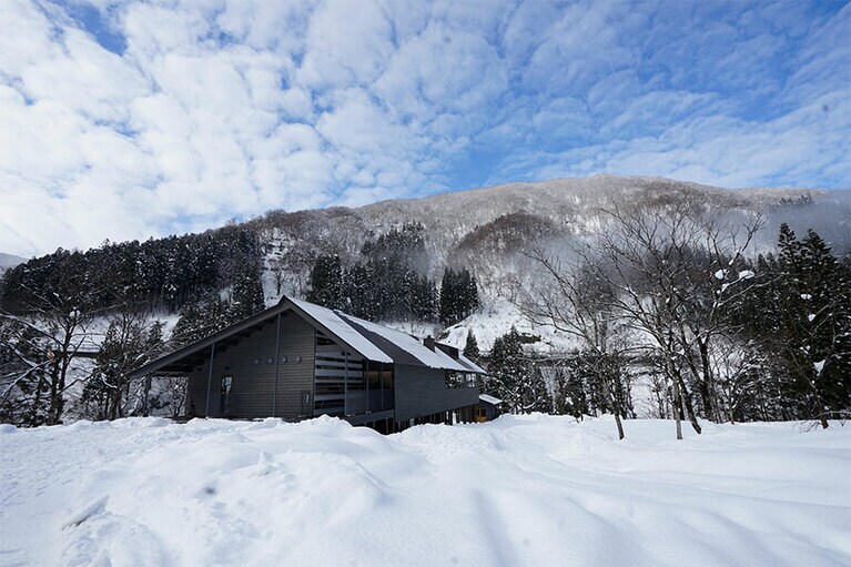 雪景色の中に佇むメイン棟。その後の谷には川が流れ、その先に山が見える。