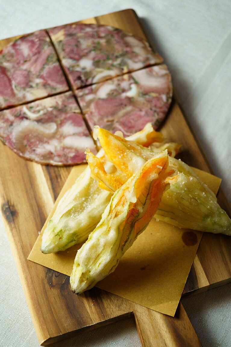 豚の頰、耳や舌などを煮込んで固めたソプラサータにズッキーニの花のフライを添えた“グランパのまな板” 12ユーロ。