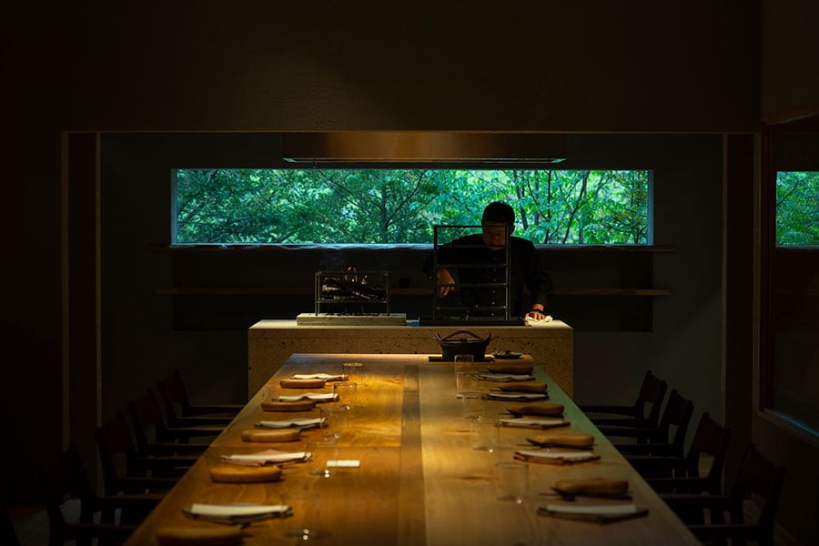 ゲストが座るテーブルの奥には、大谷石でしつらえられた薪火台で調理する豊島シェフ。調理や盛り付けする姿を間近に見ながら食事を楽しむことができる。