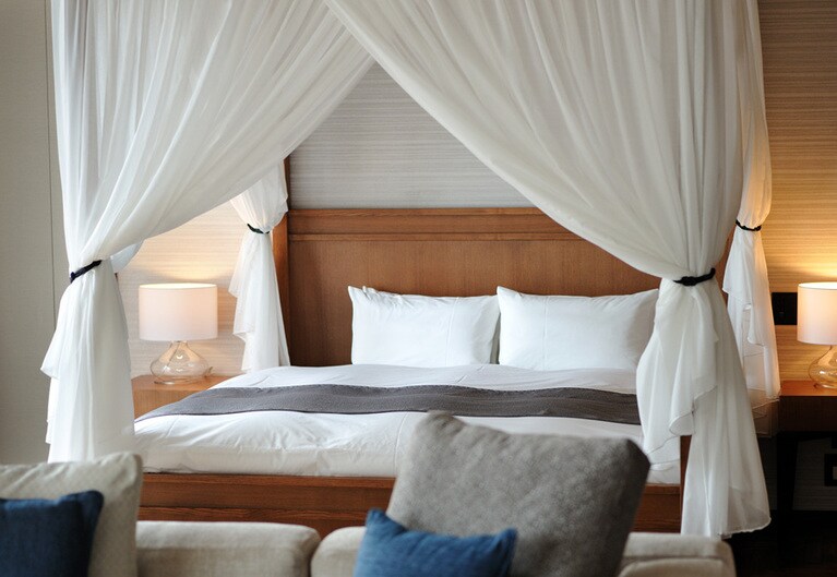 天蓋付きベッドが優雅なリゾートムードを演出するエグゼクティブルーム「プレミアムイースト」。「匠大塚」とコラボした特注家具のほか、「ACQUA DI PARMA」「Plusui」のアメニティなど、ワンランク上のこだわりが。