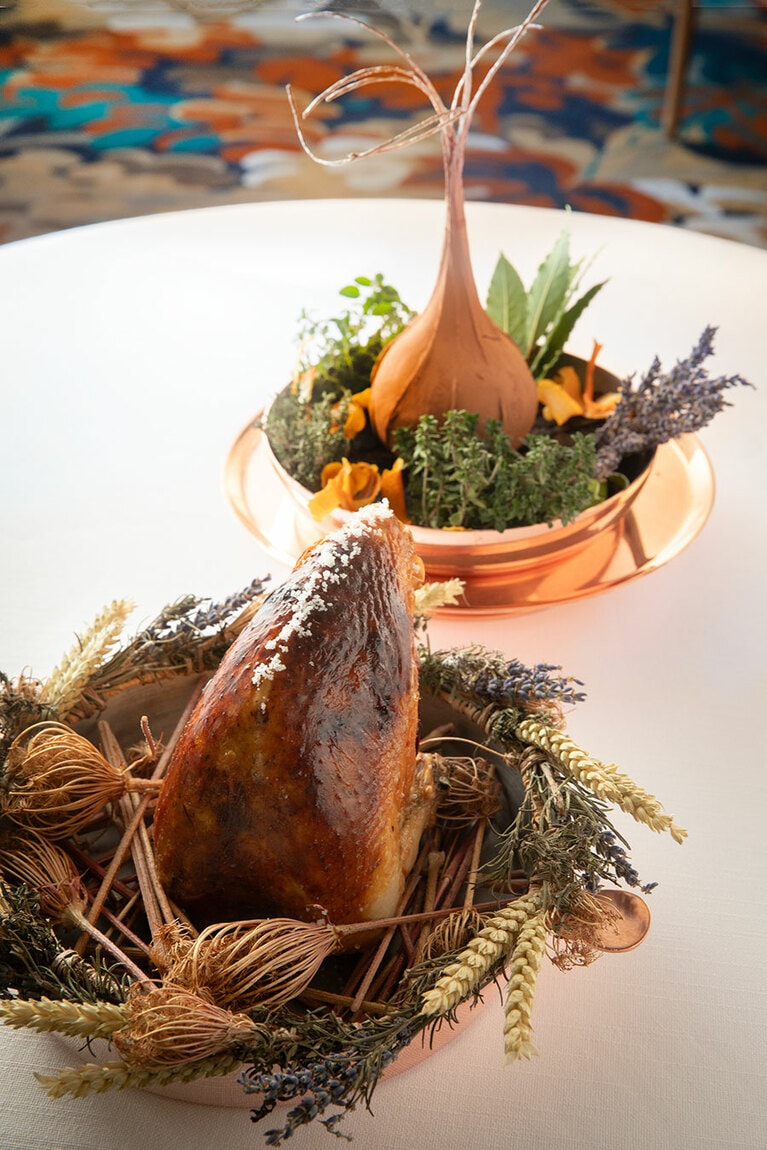 コースは290ユーロ～。スペシャリテの若鶏の料理のサービス前に、切り分ける前の素材をお客に見せる。手前は雌鶏。オレンジやレモン、コンバワなどの柑橘を効かせたバターを詰め、丸ごと焼き上げている。奥は針金で成形した粘土で玉ネギを覆い焼いたもの。