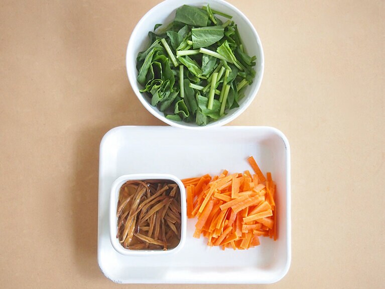 金針菜は、水（大さじ2程）で戻す。戻し汁も使うので、水を入れすぎないように注意。ほうれん草は、ざく切りにして水にさらし、アク抜きをし、人参は皮をむいて短冊に切る。