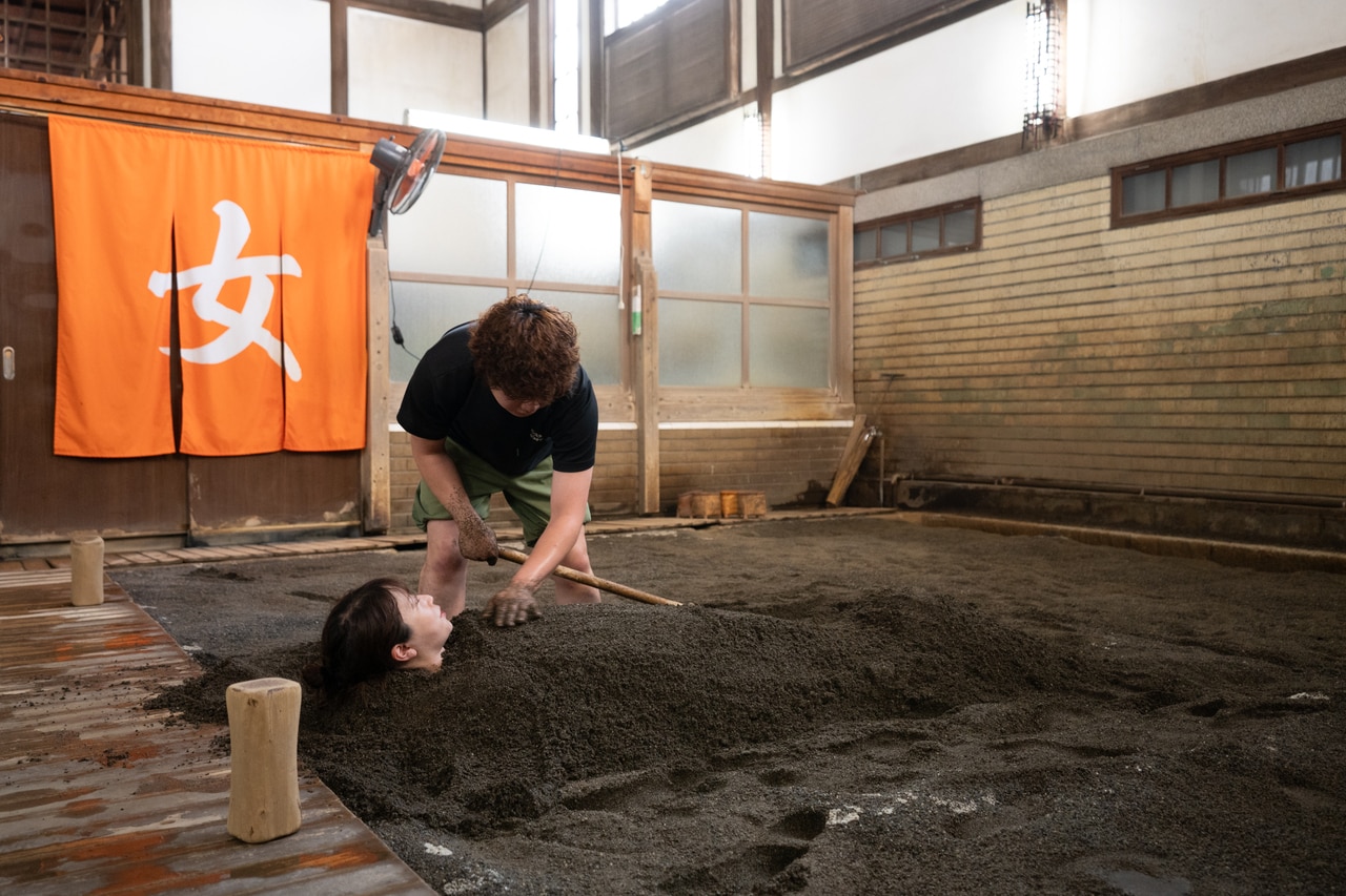 砂かけさんが全身を砂で覆う。蒸し暑い浴場内で湯を含んだ重い砂をかけるのはかなりの重労働。