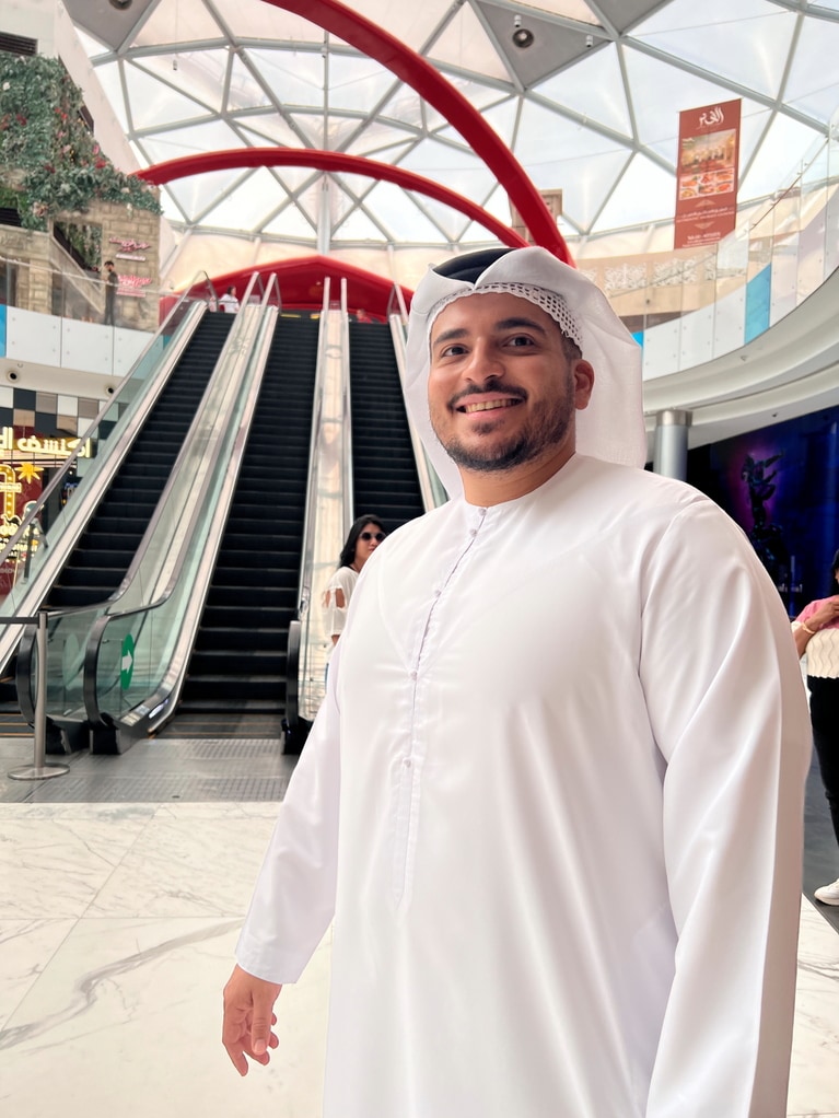 ガイドさんとウェルカムプラザで合流。カンドゥーラ（UAEの民族衣装）を着た姿に、エキゾチックなムードはMAXに！　背後のエスカレーターを上がり、陸橋を渡るとメイン棟だ。