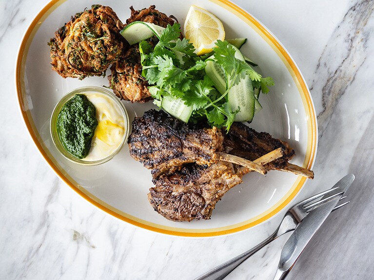 ラムチョップのマリネグリル – グリーンハリッサ＆サフランヨーグルト w/オニオンフリッター 3,200円。スパイスが芳ばしく香り、骨付きラムのジューシーな味わいが口に広がる男性にも喜ばれるディナーメニュー。中東のスパイスやサフランを加えたヨーグルトソースはピリっと辛く身体の中から温まる。bills 銀座限定。