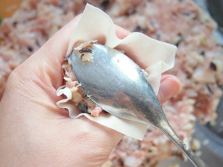 (4) 親指と人差し指の先をくっつけ、円を作ったら上に焼売の皮をのせます。(3)の肉ダネを適量置いて、焼売の形に整えます。