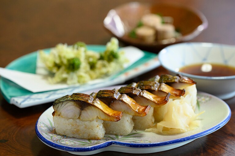 地酒のあてとして、締めのごはんとしても喜ばれる「焼鯖棒寿司」1000円。奥は「蕗の薹天ぷら」700円と「かわはぎ肝ポン酢」700円。