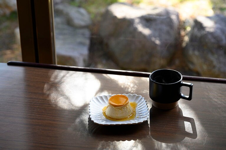 ときおりトキの舞う姿も見ることができる窓際の席。クリームをたっぷり使用した当カフェ自慢の「自家製 Tono プリン」400円。「本日のコーヒー」（今回はパナマ）350円。