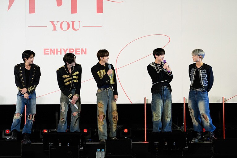 両手でマイクを握り、赤い糸の意味について語るSUNOOと、SUNOOを見つめるJAY。