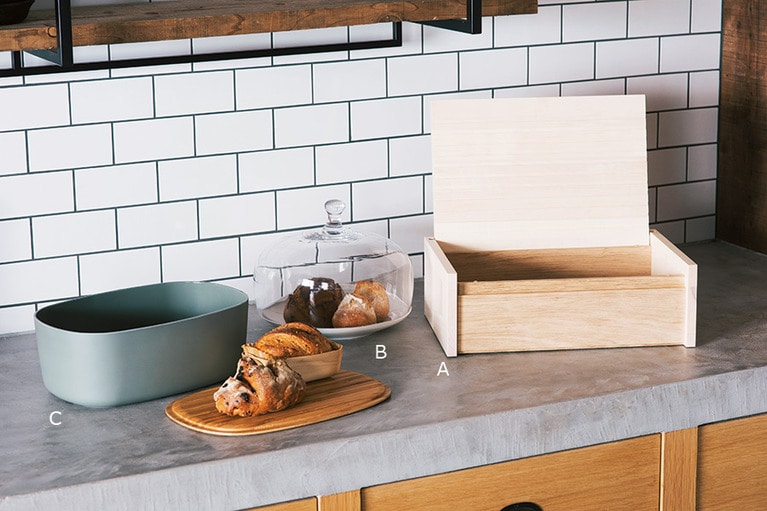 A. 程よい湿度が保てる無塗装の木製ボックス。ブレッドボックス 20,000円／サイド バイ サイド(スコープ)。 B. フィンランドで人気のライフスタイルブランドによる吹きガラスのケーキカバーをパンの保存用に。カバー 8,000円、プレート 4,500円／ペンティック(スキャンデックス)。 C. 蓋の裏はカッティングボード仕様。パンを取り出しからサーブまでスムーズに行える。ブレッドボックス 8,800円／リグティグ(スキャンデックス)