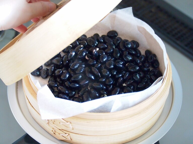 蒸し器にクッキングシートを敷き、黒豆を並べる。湯を沸騰させ、蓋をして弱火で約1時間蒸す。
