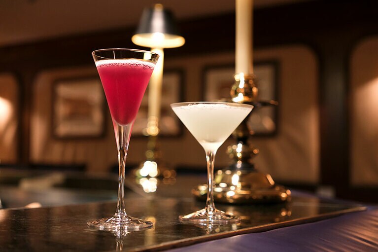 「マリナーズクラブ」の人気カクテル。左から、現在の飛鳥Ⅱ船長の好む日本酒やジュースを用いた“キャプテンズカクテル”1,100円、飛鳥Ⅱオリジナルのジンをベースにパイナップルやミントが香る“ワールドクルーズ”1,650円。