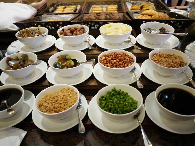 ザーサイ、たくわん、ゆでピーナッツ 、塩卵、揚げ葱などの薬味が用意されていて、好きにトッピングができる。薬味は味のアクセントになるよう塩気の強いものが多く、お粥との相性はばっちり(写真提供：まゆこさん)。